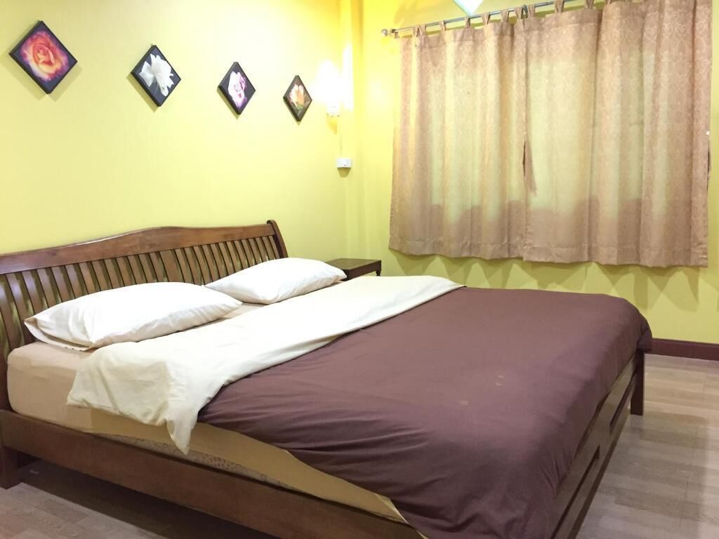 A single bed with a wooden headboard, a brown mattress, and white pillows. There are three wall-mounted light fixtures and a window with beige curtains.