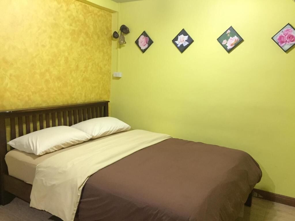 A bed with a brown cover and white pillows, a wooden headboard, and a yellow wall with four framed pictures of flowers.