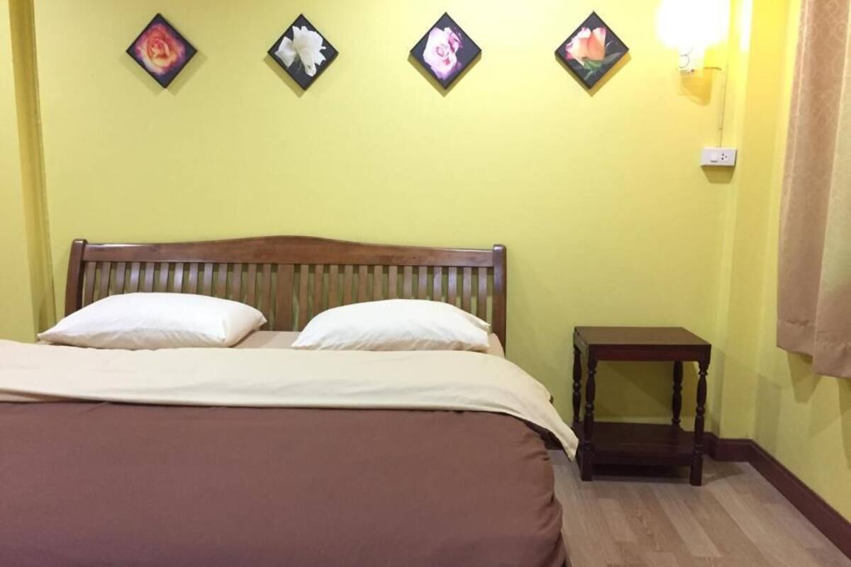 Una cama con cabecera de madera, una mesita de noche y cuatro cuadros de flores colgados en la pared.
