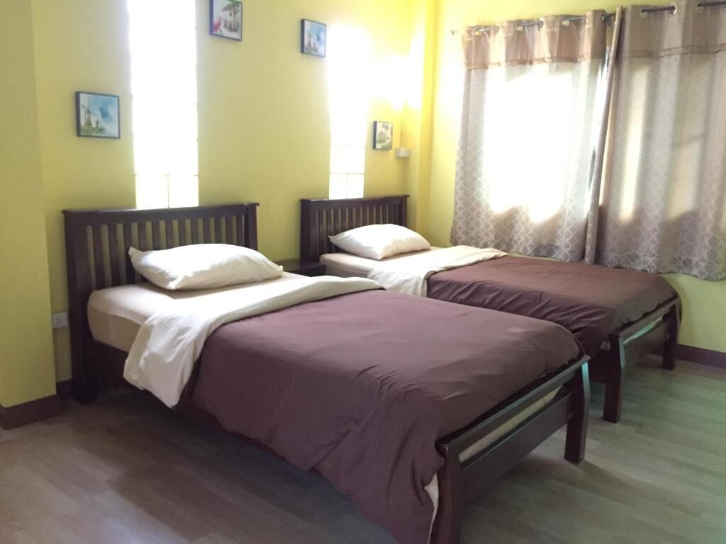 Een kamer met twee bedden, houten hoofdeinden en een raam met gordijnen.