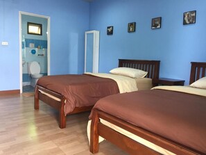 A room with two wooden beds, a blue wall, and a door leading to a bathroom. - Baan Bussara (Ayutthaya)