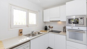A modern kitchen with white cabinets, stainless steel appliances, a double sink, and a window with blinds. - Townhouse in Llafranc - Costa Brava (Llafranc)