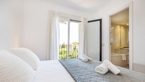 A hotel room with a bed, a balcony with curtains, and a bathroom visible through an open door. - Townhouse in Llafranc - Costa Brava (Llafranc)