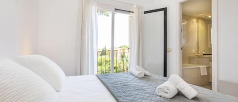 A hotel room with a bed, a balcony with curtains, and a bathroom visible through an open door.
