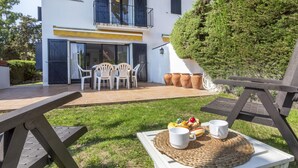 A patio with outdoor seating, a table with a placemat, and a view of a white building with blue shutters and a yellow awning. - Townhouse in Llafranc - Costa Brava (Llafranc)