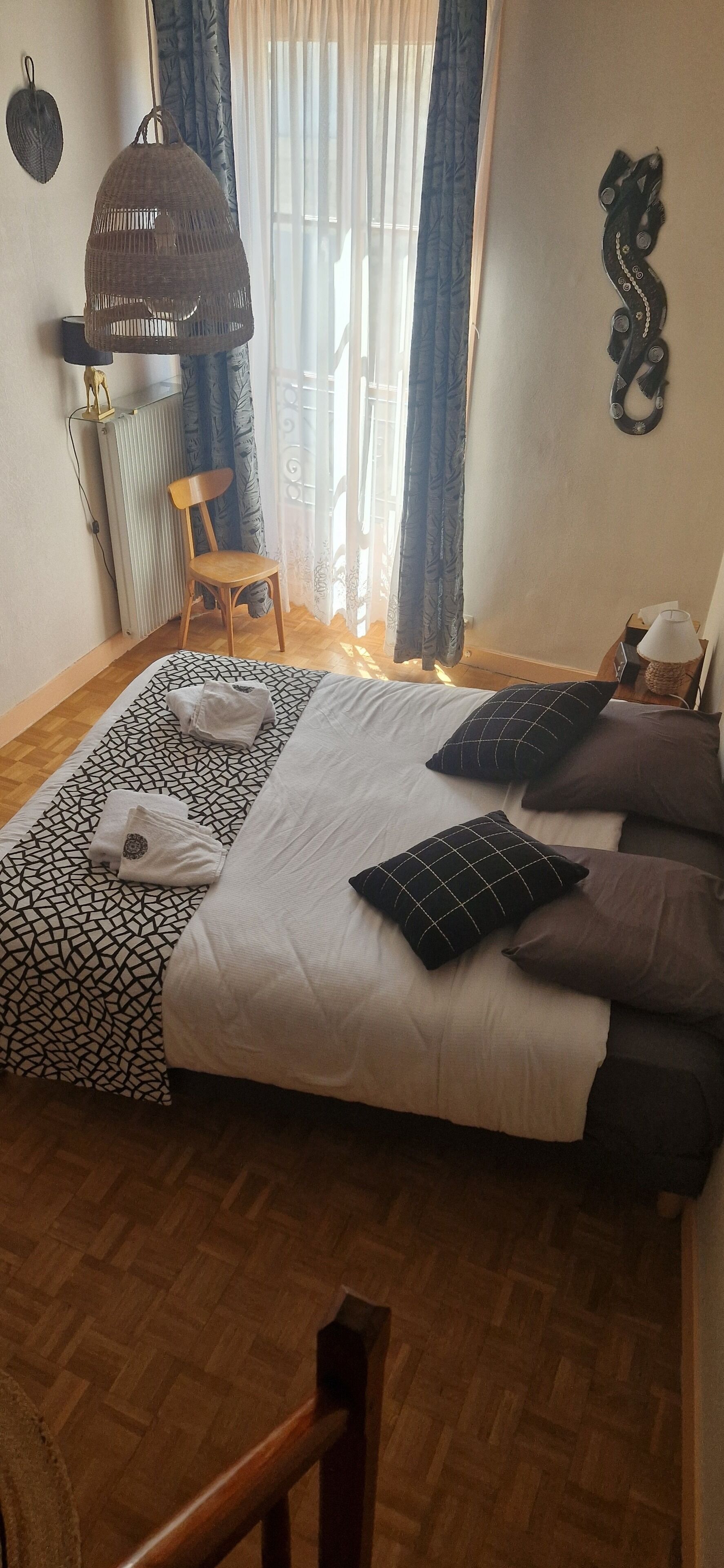 A neatly arranged bedroom with a bed, pillows, a chair, a hanging light fixture, and a radiator.