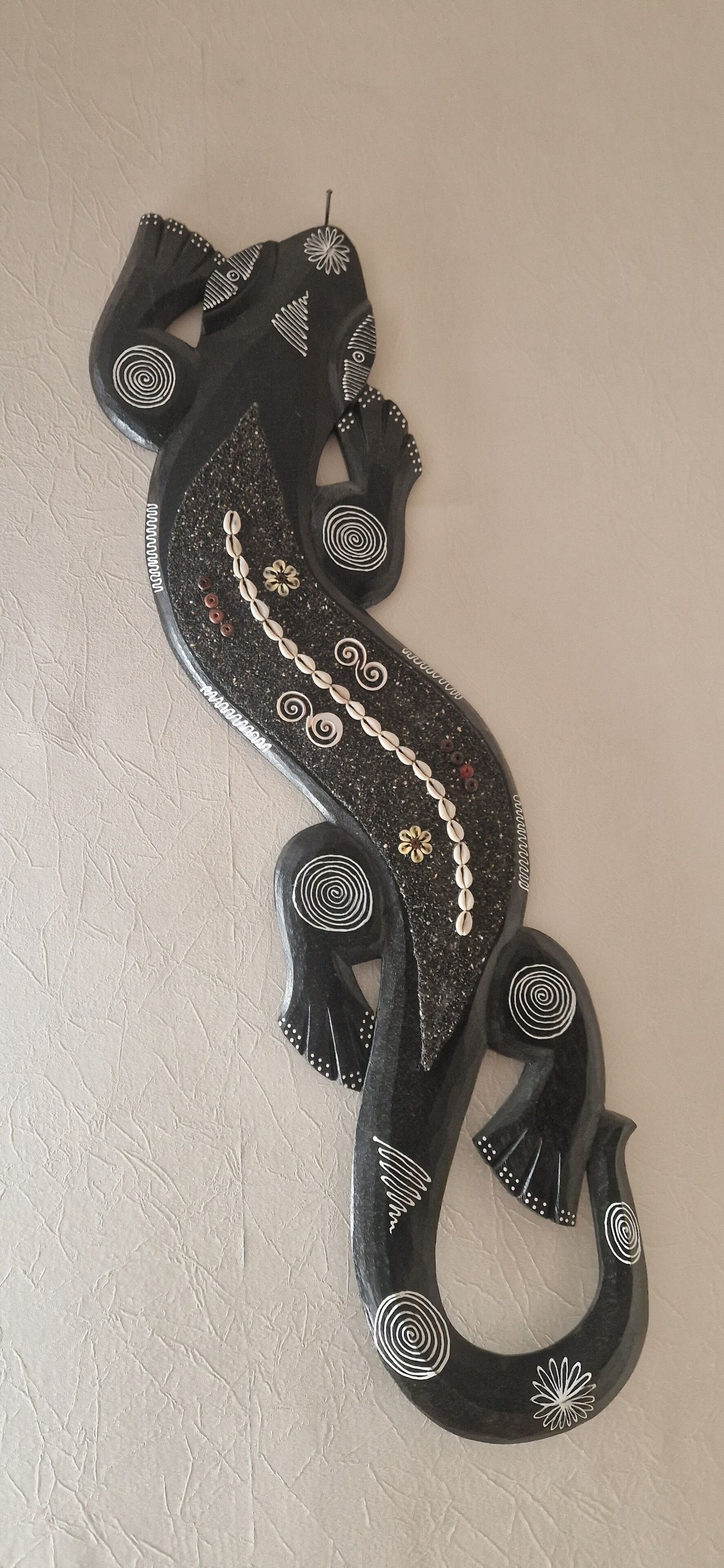 Un élément décoratif mural, fixé au mur, arborant un motif serpentin et agrémenté de motifs circulaires et floraux.