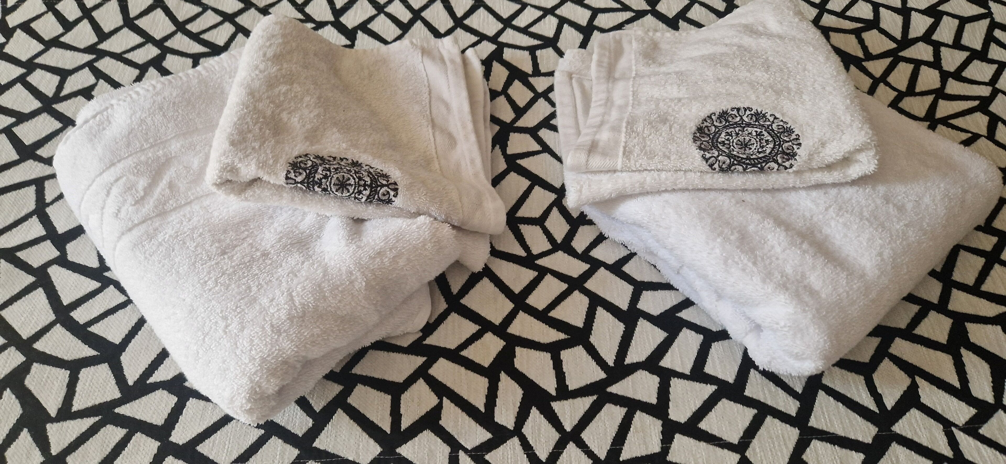 To sammenfoldede håndklæder med detaljeret sort broderi på et mønstret stof.