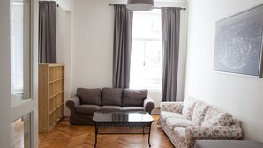 A living room with a brown sofa, a floral sofa, a glass coffee table, and a wooden shelving unit. - 2 Bed Flat - Sleeps 9 - Pets - Smoking on terrace (Praha)