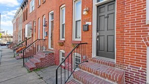A row of red brick townhouses with numbered doors, front steps, and a clear sidewalk. - Charming Baltimore Townhome w/ Scenic Views (Baltimore)
