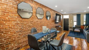 A room with a brick wall, a dining table with chairs, a TV, and a sofa. - Charming Baltimore Townhome w/ Scenic Views (Baltimore)