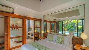 A modern bedroom with a large bed, a desk, and a chair, a large mirror, and a view of a swimming pool. - Villa Anahata (Seminyak)