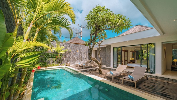 A modern pool area with lounge chairs, a stone wall, and lush greenery. - Villa Anahata (Seminyak)