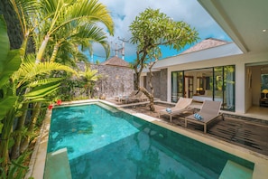A modern pool area with lounge chairs, a stone wall, and lush greenery. - Villa Anahata (Seminyak)