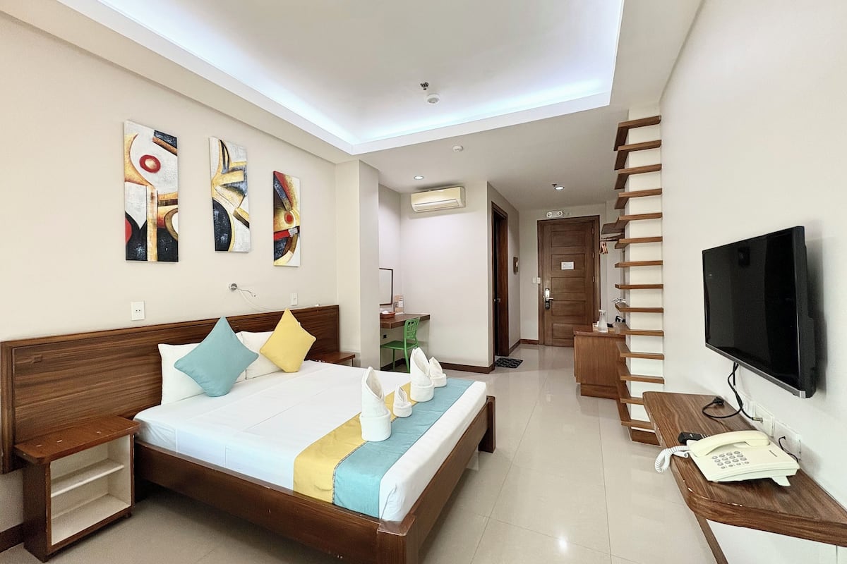 Habitación de hotel con cama, mesitas de noche, televisión, teléfono y obras de arte en las paredes.
