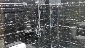 A modern bathroom with black marble walls, a white toilet, and a glass-enclosed shower area. - Sunburn Suites Coron (Coron)
