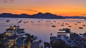 A coastal village at sunset with boats on the water, houses with thatched roofs, and a pier extending into the sea. - Sunburn Suites Coron (Coron)