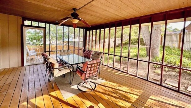 Eine überdachte Terrasse mit Tisch, Stühlen, großen Fenstern und einem Deckenventilator.