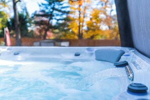 A hot tub with water jets, surrounded by a wooden fence and trees with autumn foliage.