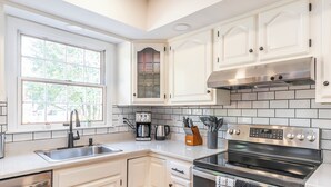 Una cucina moderna con mobili bianchi, piano cottura in acciaio inossidabile e macchina da caffè.