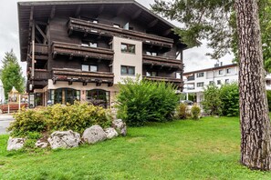 Un edificio a più piani con balconi, un cartello con su scritto 'TRAGIA' e un prato curato con rocce e alberi.