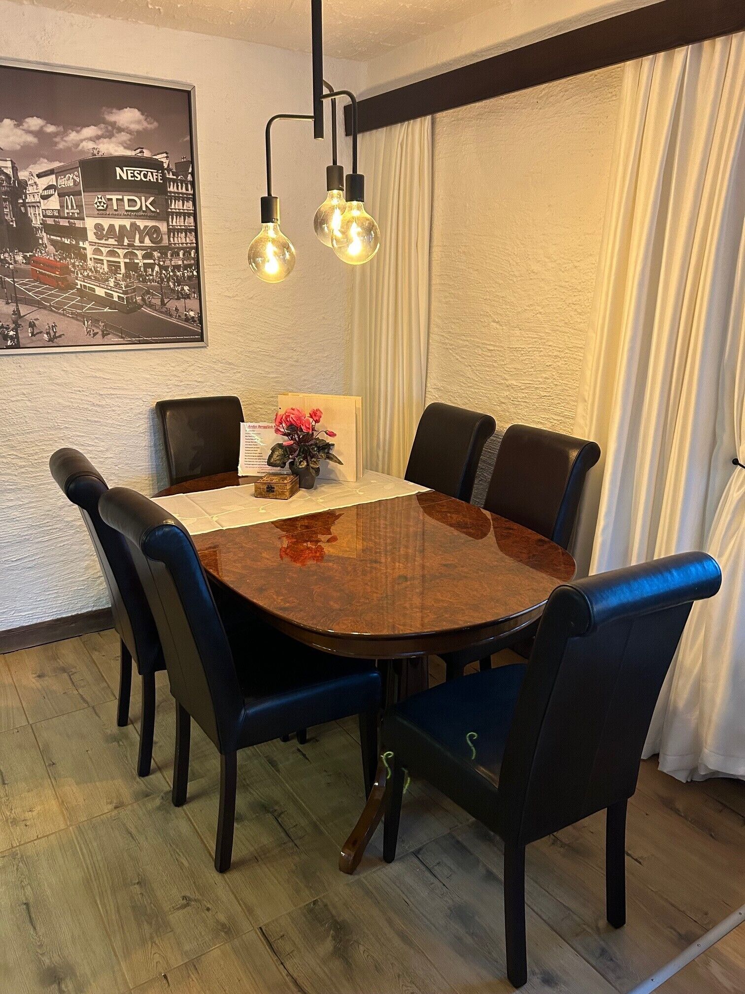 Ein Essbereich mit einem runden Tisch, schwarzen Stühlen, einer Blumenvase, einem gerahmten Bild an der Wand und einer Hängelampe.