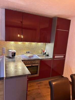 Una cucina compatta con mobili rossi, un forno a microonde, un tostapane e un lavandino.