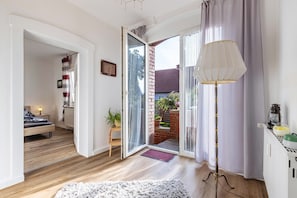 Une pièce comprenant un lit, une lampe sur pied, une petite table et une porte-fenêtre coulissante donnant sur un espace extérieur agrémenté de plantes.