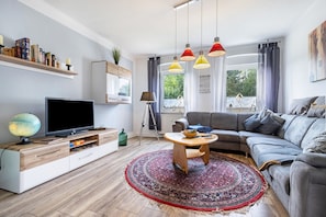Un salon moderne avec un téléviseur à écran plat, un meuble de rangement en bois, un canapé gris et un tapis à motifs.