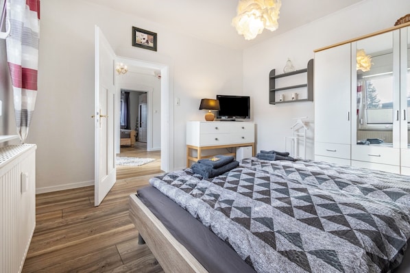Une chambre à coucher comprenant un lit, une télévision, une commode, une armoire et une porte donnant sur une autre pièce.