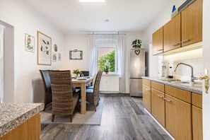 A compact kitchen with wooden cabinets, a dining area with wicker chairs, and a view of greenery outside.