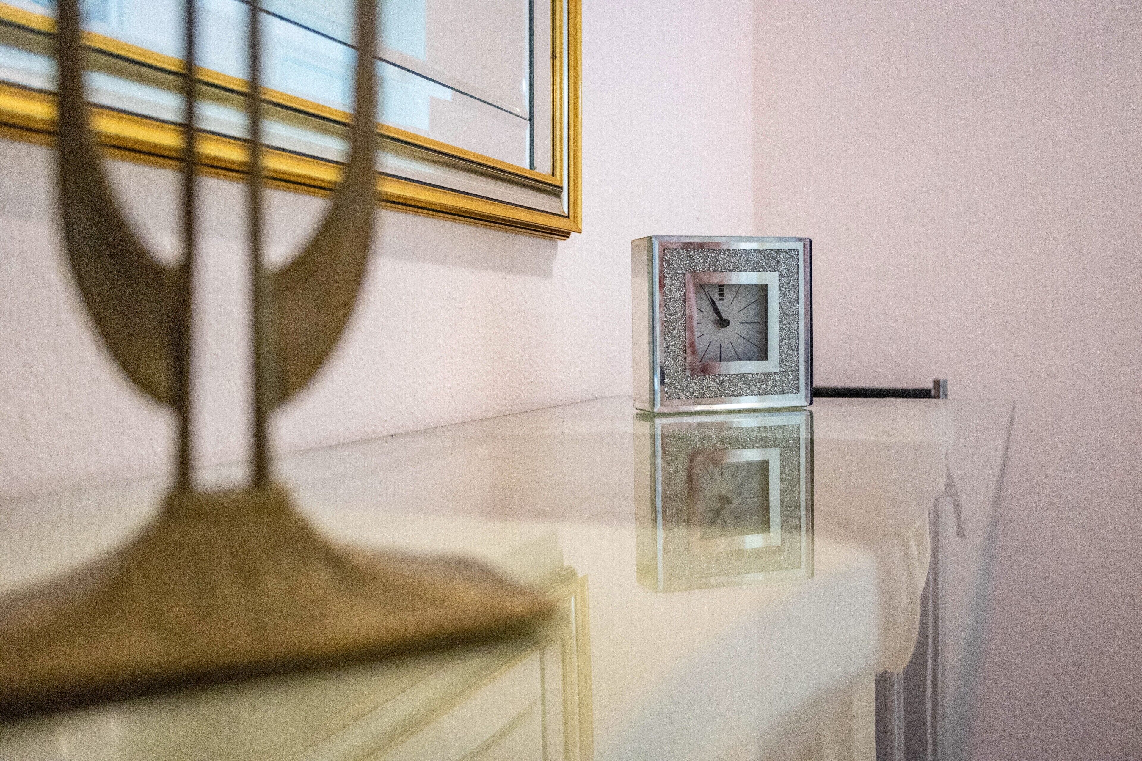 Eine Uhr auf einer spiegelnden Oberfläche, ein gerahmtes Bild an der Wand und ein Fenster mit Blick.