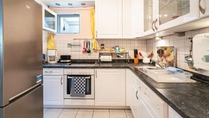 Eine kompakte Küche mit weißen Schränken, einem Edelstahl-Kühlschrank, einer Mikrowelle und einem eingebauten Backofen.