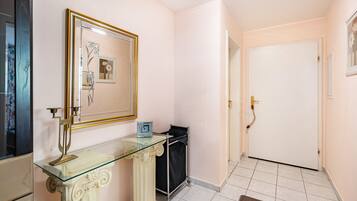 Um corredor com uma mesa consola de vidro, um quadro emoldurado, uma porta e chão revestido de azulejos.
