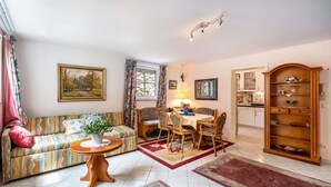 Ein Wohnzimmer mit Sofa, Esstisch mit Stühlen, Küchenzeile und Bücherregal.