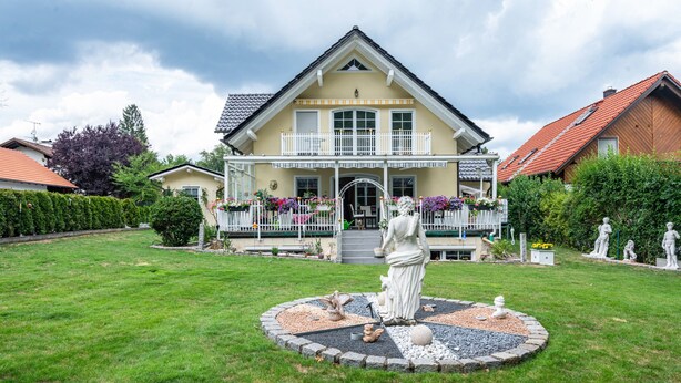 Ein zweistöckiges Haus mit einem Balkon, einem Garten mit einer Statue und einem gepflegten Rasen.