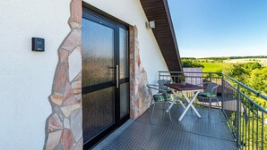 A balcony with a stone wall, a sliding glass door, a metal table, and a chair. - Holiday Apartment "Hügelblick Oase" with Shared Garden, Balcony & Wi-Fi (Kraichtal)