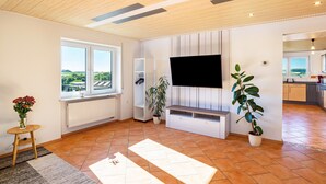A modern living room with a large window, a flat-screen TV, a white entertainment unit, and a potted plant. - Holiday Apartment "Hügelblick Oase" with Shared Garden, Balcony & Wi-Fi (Kraichtal)
