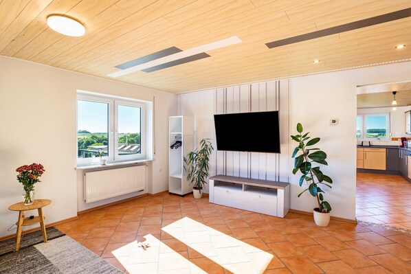 A modern living room with a large window, a flat-screen TV, a white entertainment unit, and a potted plant.