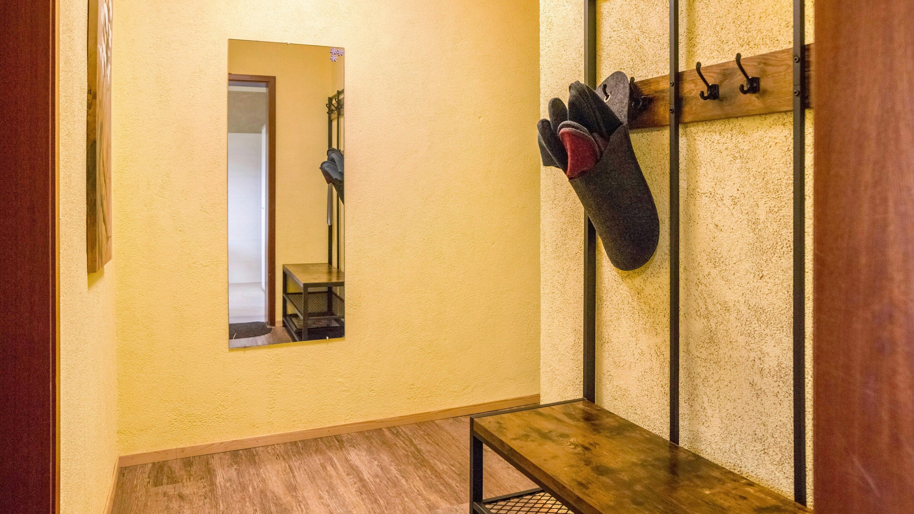Un couloir avec un banc en bois, un porte-manteau avec des gants, un miroir et une porte donnant sur une autre pièce.