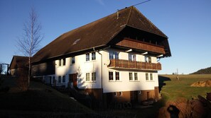 A two-story building with a sloped roof, a balcony on the upper floor, and a small porch area.