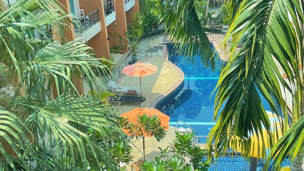 Un resort con piscina, palme e un edificio con balconi.