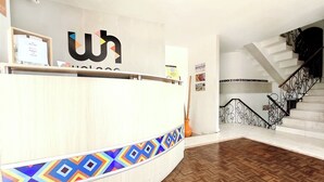 A reception desk with a geometric patterned border, a staircase with ornate railings, and a herringbone wooden floor. - Walena Hotel (Riohacha)