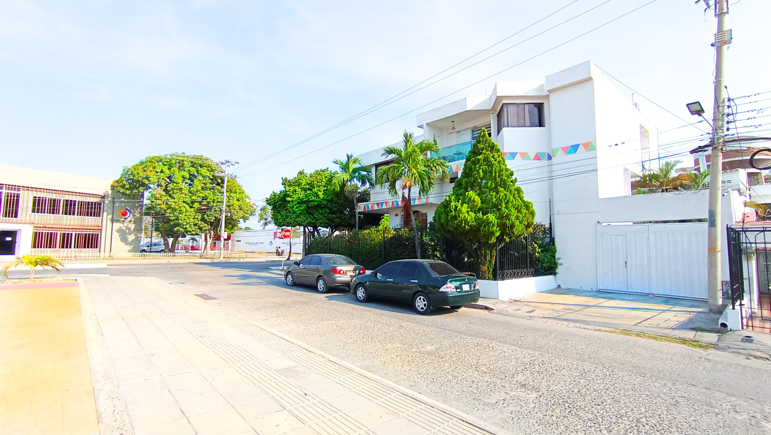 A street view with two cars parked on the side, buildings with balconies, and a clear sky.