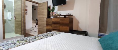 A bedroom with a bed, a dresser, a television, and a bathroom visible through an open door.