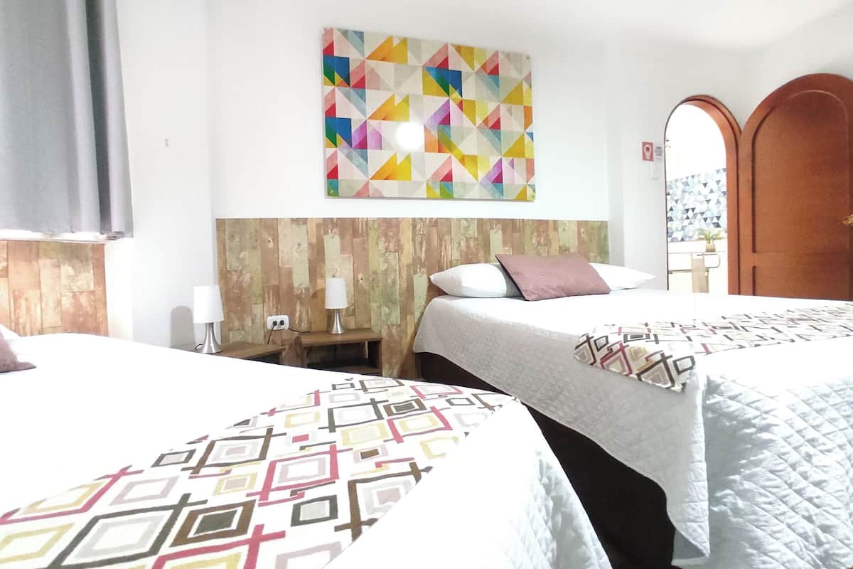 A hotel room with two beds, a wooden headboard, a colorful geometric wall art, and a door with a geometric pattern.