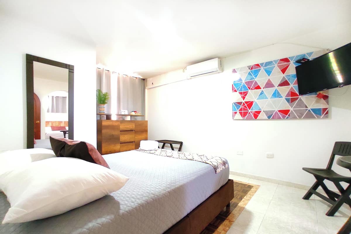 A bedroom with a bed, a dresser, a chair, a TV, and a geometric wall art piece.