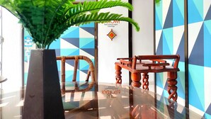 A modern interior with a glass table, wooden chairs, and a large green plant. - Walena Hotel (Riohacha)