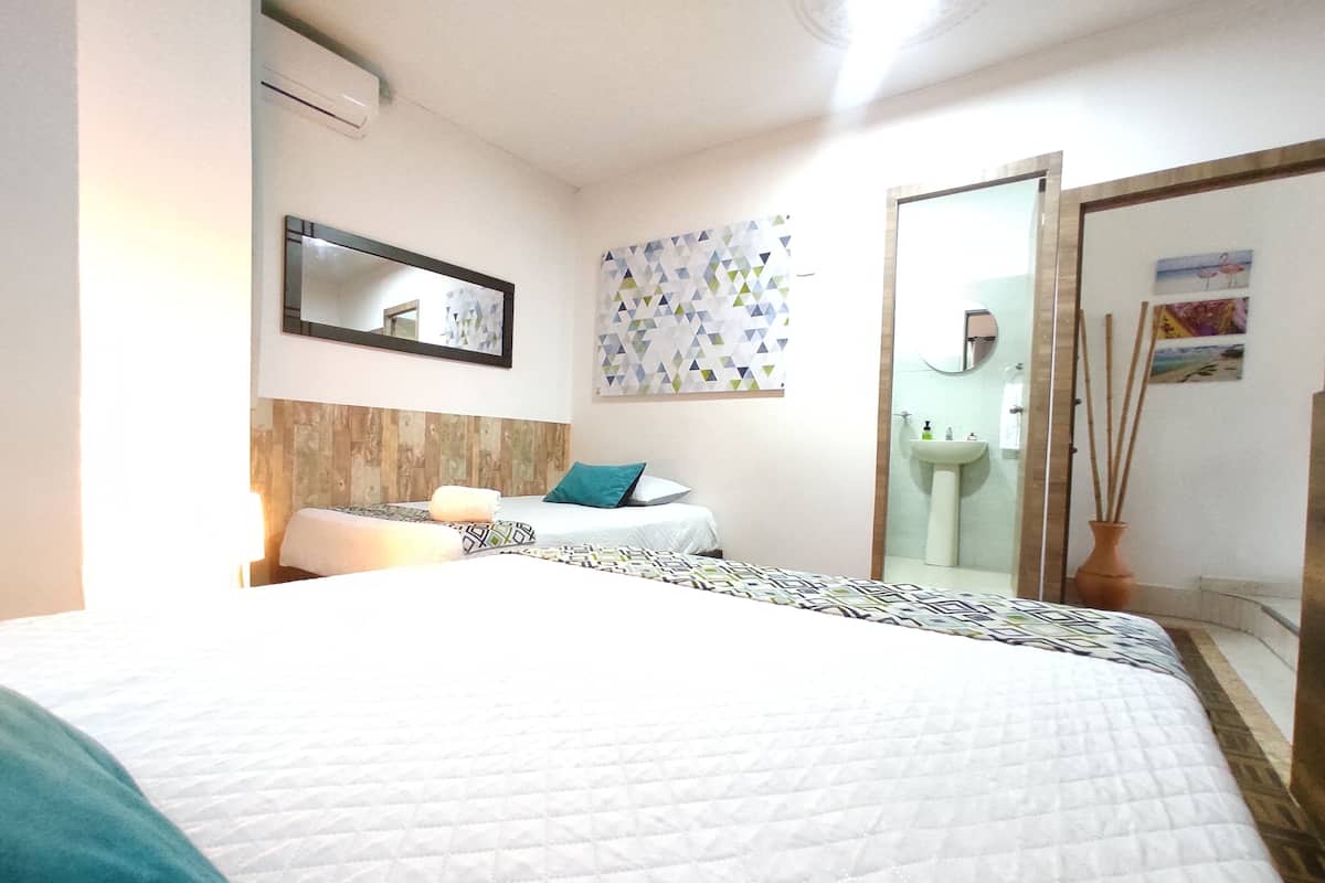 A hotel room with a bed, a bedside table, a mirror, a bathroom with a sink and mirror, and a wall with geometric artwork.