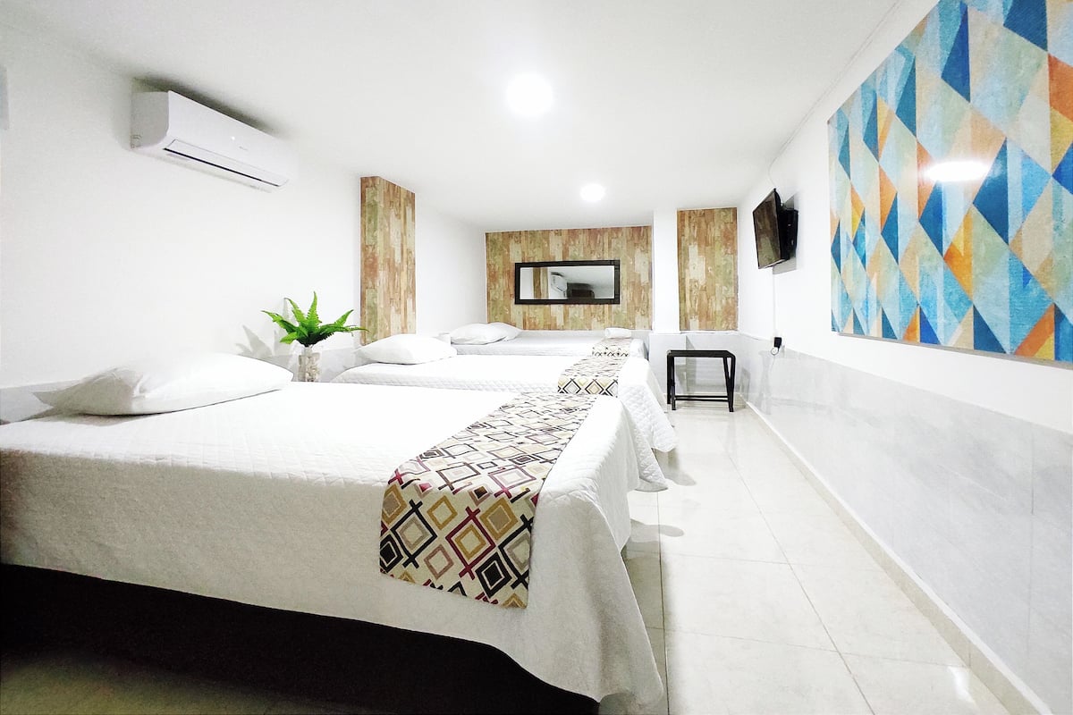 A hotel room with two beds, a small table, a mirror, and a TV on the wall.